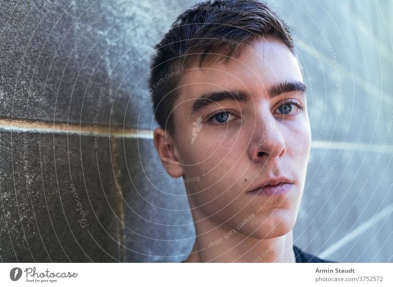 portrait of a serious young man leaning against a wall closeup sad worried cool standing grunge confident dirt outdoor teenager looking male beautiful casual