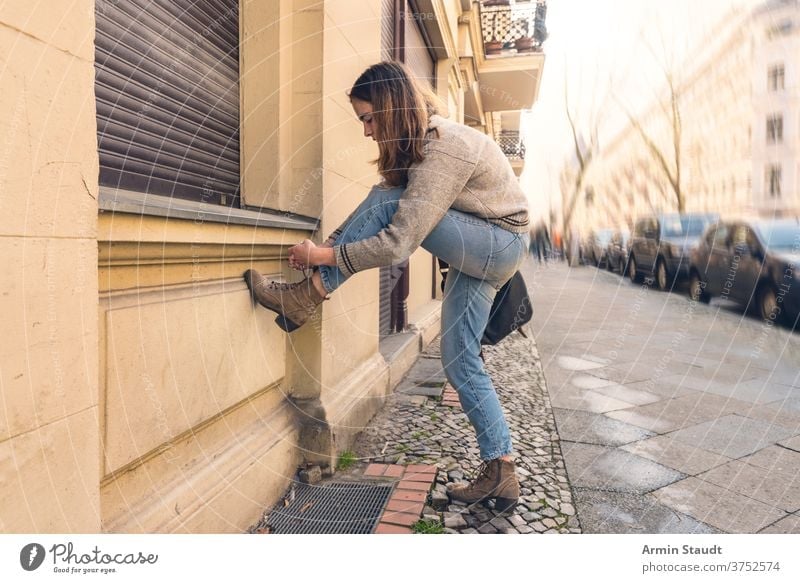 young woman ties her shoe on the street portrait outdoor pavement cars city town urban crouching shoes summer beautiful concentrated bag wall brick Berlin