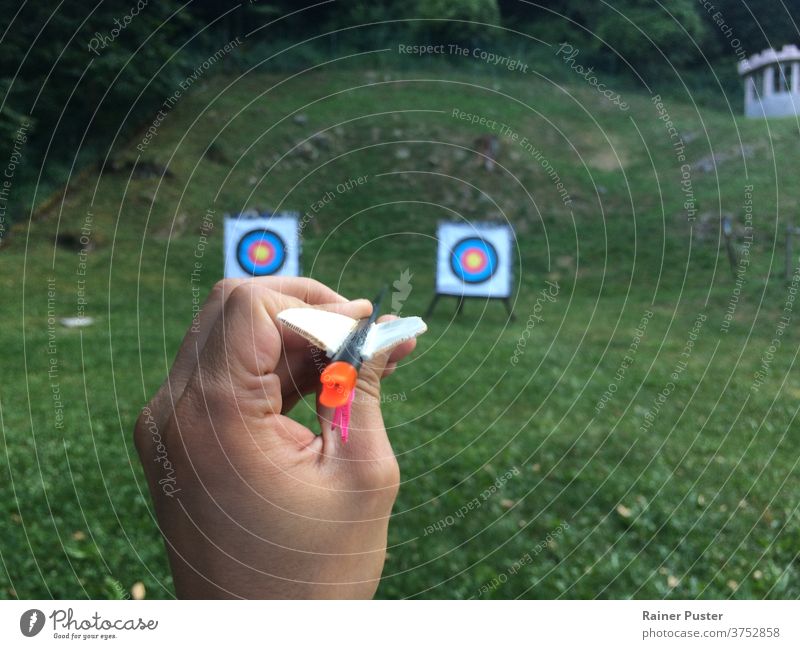 Hand holding an arrow with two targets in the background alternatives archer bow business strategy decision finger focus fun gadget game goal goal-oriented