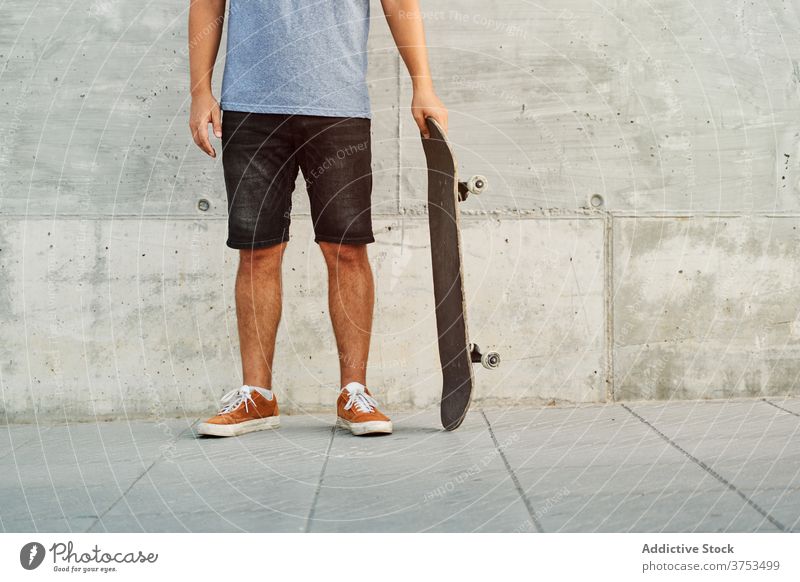 Crop skater standing on street man skateboard city street style trendy outfit urban building male pavement sidewalk modern contemporary cool hobby hipster guy
