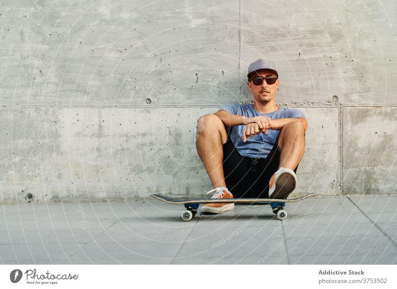 Stylish man with skateboard in city skater urban building style hobby skill lean wall male outfit confident trendy street modern young sit cool hipster fashion
