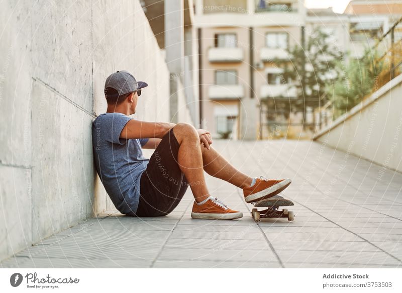 Stylish man with skateboard in city skater urban building style hobby skill lean wall male outfit confident trendy street modern young sit cool hipster fashion