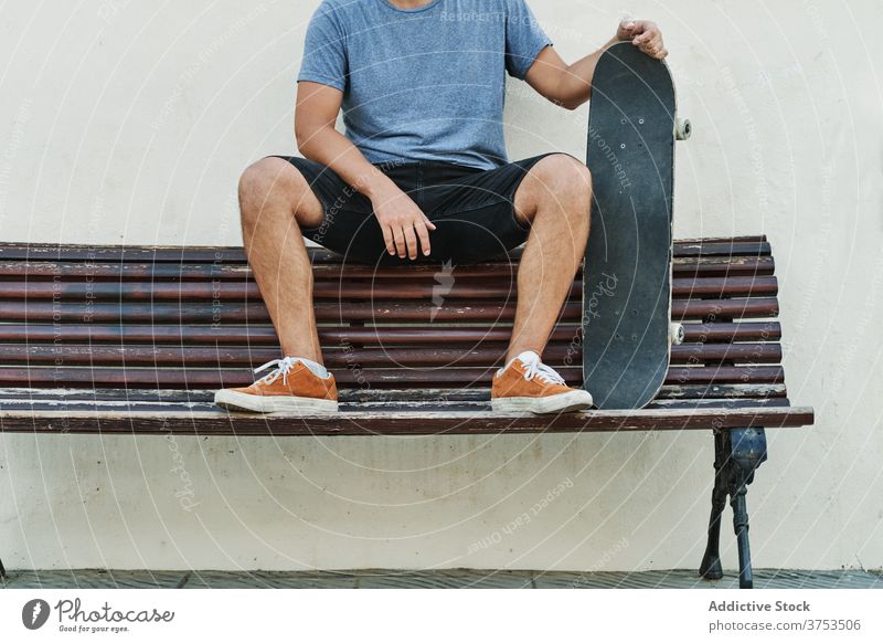 Crop skater sitting on bench in city urban skateboard man relax style street cool generation male young shabby wooden rest trendy hobby town modern hipster