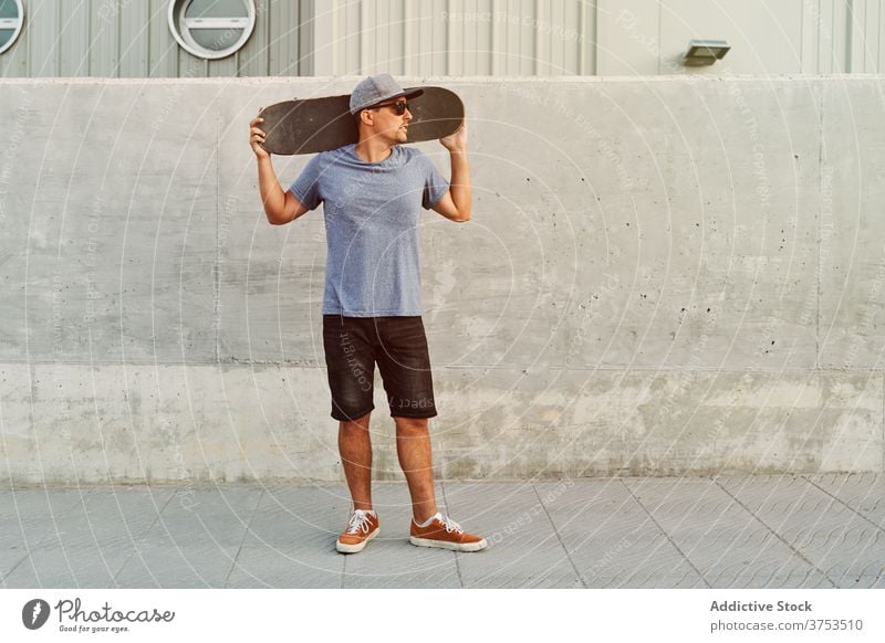 Confident man with skateboard near building city skater determine style hobby trendy urban street male sunglasses outfit modern stand cool young hipster