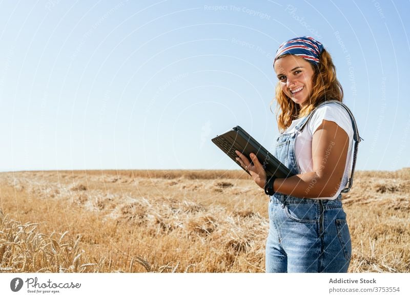 Smiling woman using tablet in field farmer wheat browsing agriculture countryside rural female gadget device summer nature meadow plantation farmland harvest