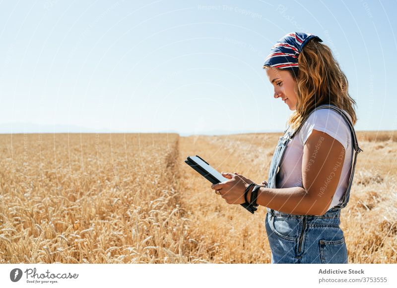 Smiling woman using tablet in field farmer wheat browsing agriculture countryside rural female focus gadget device summer nature meadow plantation farmland