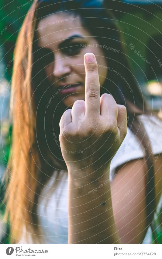 Young woman looks angrily into the camera and gives the finger Give the finger rabid Woman brunette Middle finger Sour agressive quarrel Conflict Emotions