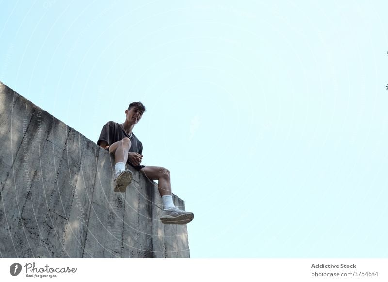 Young man sitting on stone border in city wall relax parkour building concrete high skill male rest training smile young cheerful urban exterior facade