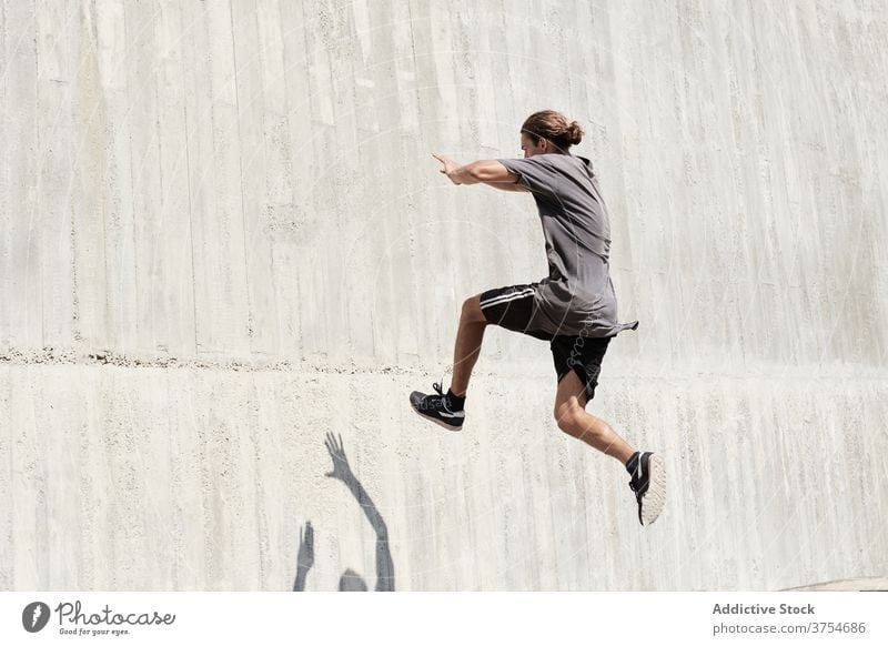 Strong man jumping on wall of building parkour stunt freestyle trick urban city extreme danger male street courage young active handsome activity professional