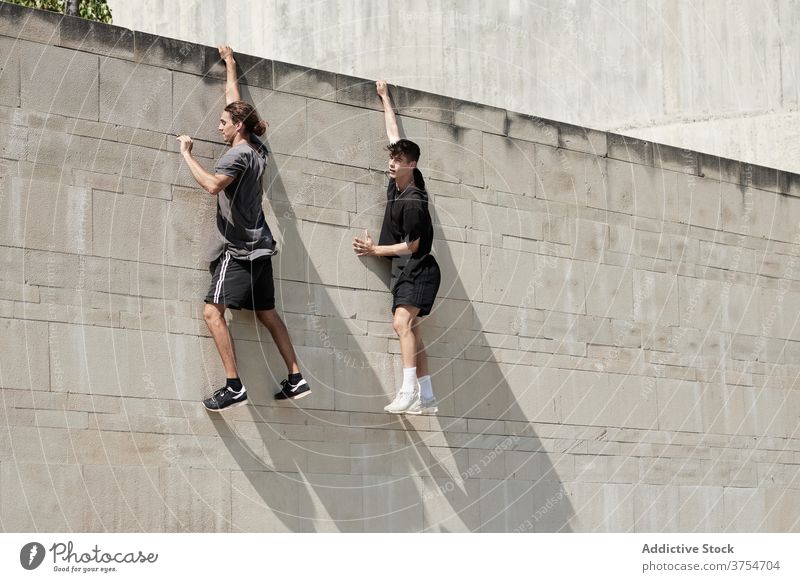 Strong men hanging on wall of building parkour freestyle risk stunt urban together extreme trick city danger courage young active handsome activity professional