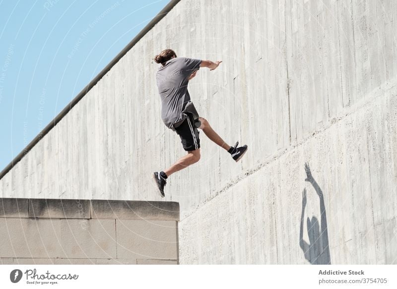 Strong man jumping on wall of building parkour stunt freestyle trick urban city extreme danger male street courage young active handsome activity professional