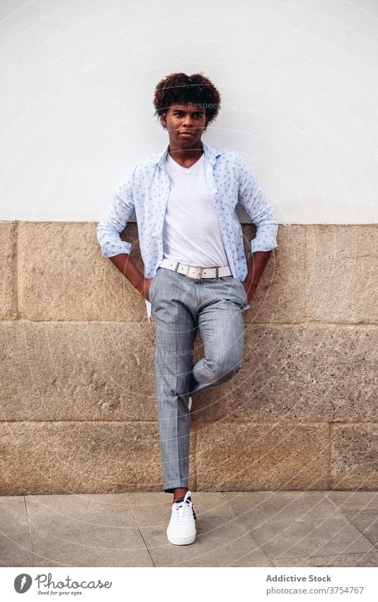 Confident man in stylish wear in city style trendy modern street posture unemotional building wall male ethnic black african american appearance hairstyle afro