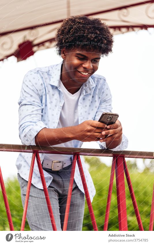 Happy black man standing in city observe summer street metal railing browsing watching smartphone male ethnic african american outfit trendy confident town rest