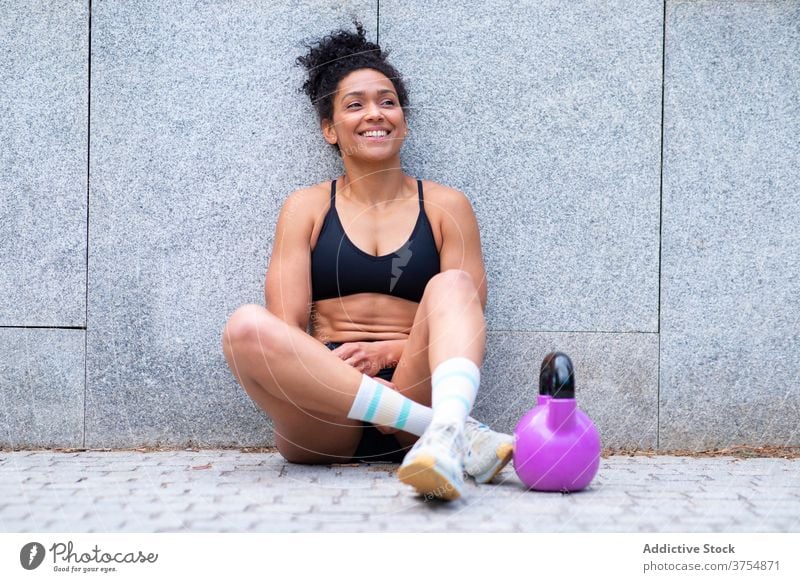 Content ethnic sportswoman resting during training functional relax break city kettlebell workout smile fit female black african american athlete sportswear