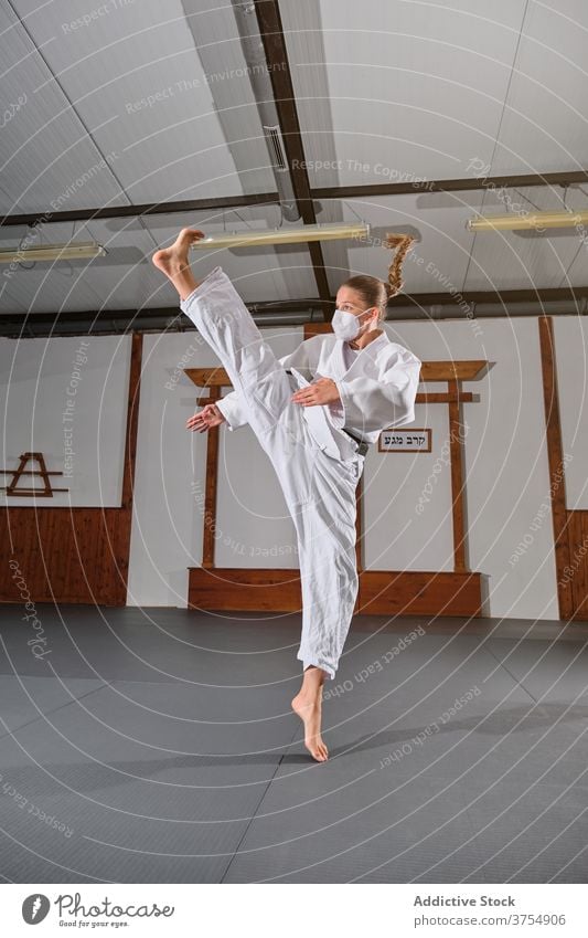 Woman with a white kimono kicking in the air posture balance powerful trainer wellbeing practice skill strength sports uniform wellness position confident