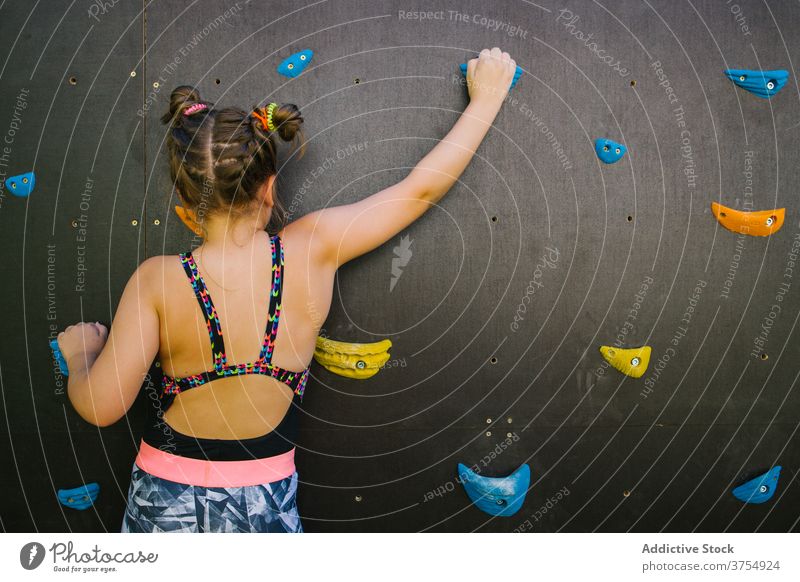 Courageous girl climbing wall in gym child boulder brave artificial rock grip training balance hold fearless practice exercise extreme hobby challenge sport kid