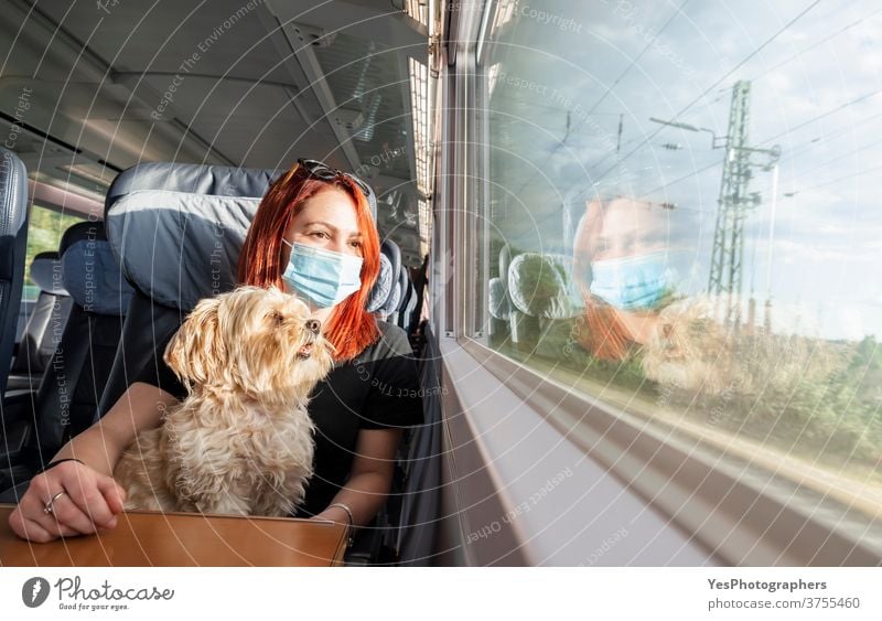Young woman with face mask and dog traveling by train.Train travel during pandemic Germany Millennial adventure business class carriage caucasian chairs