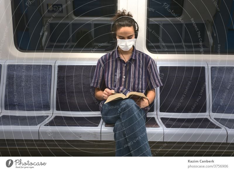 Concentrated masked millennial reading a book and listening to music in subway metro underground headphone sitting man young student teenager university college
