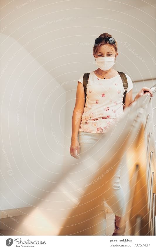 Woman going downstairs wearing face mask to cover mouth and nose during pandemic coronavirus outbreak woman pharmacy covid-19 female care indoor person protect