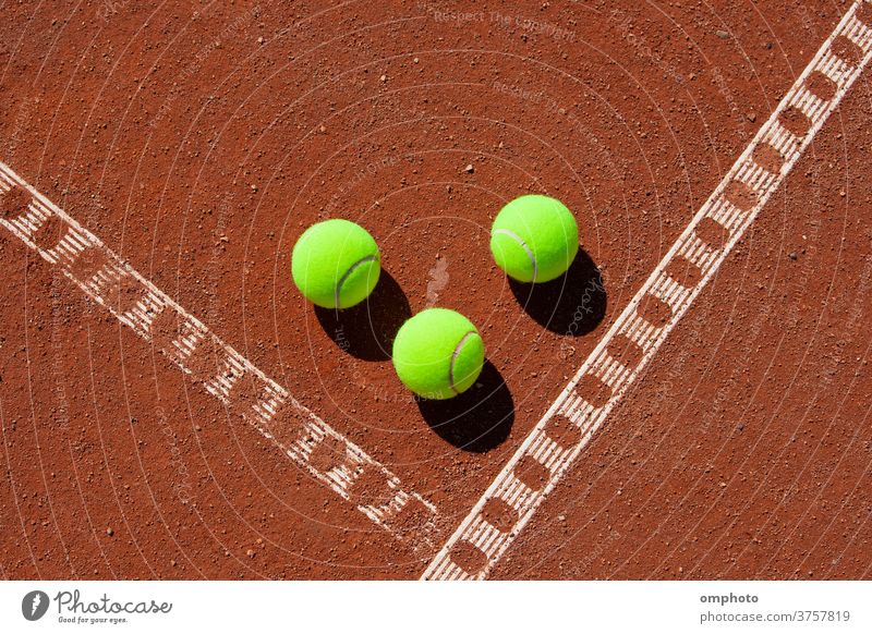 Three tennis balls in the corner of a clay field court line game red ground orange sport activity white outdoor set competition play exercise equipment