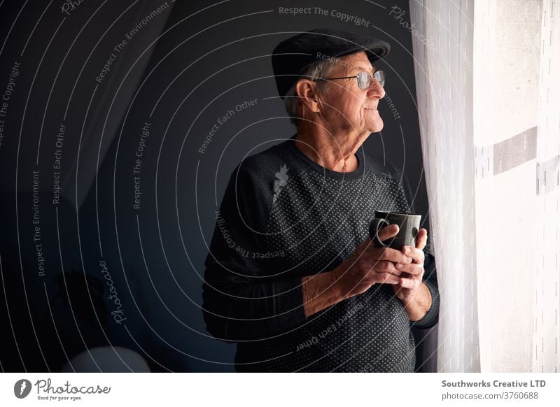 Senior man smiling out of window senior male hat glasses home happy looking copy space retired coffee mug cup waiting mature pensioner indoors lonely eyeglasses