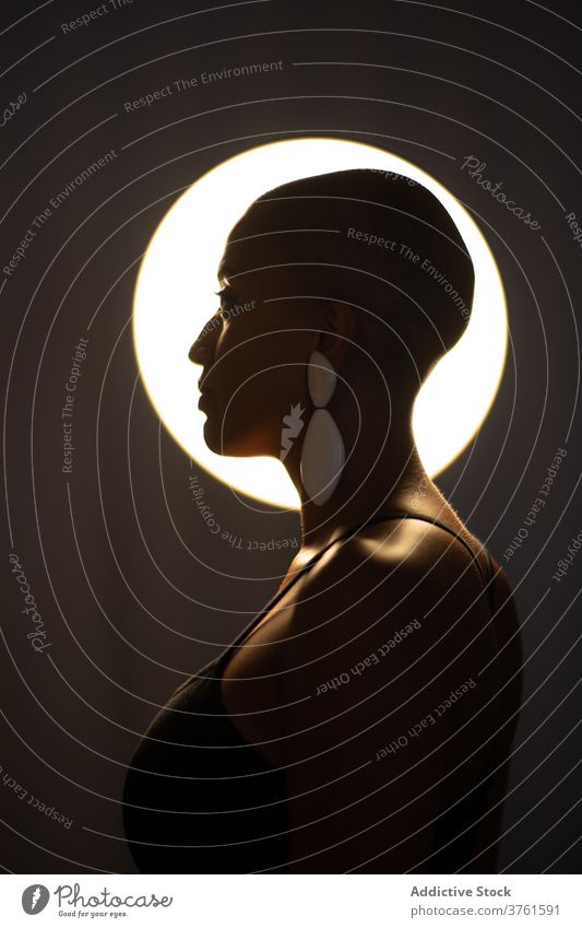 Stylish ethnic woman in dark studio style lamp illuminate trendy bald hairstyle appearance female black african american confident serious fashion charming glow