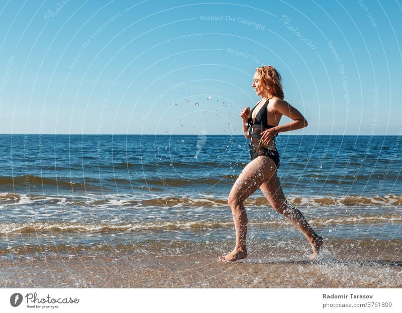 young blonde girl in a black swimsuit runs along the sand of the sea shore beauty caucasian body beautiful model female water ocean person woman summer bikini