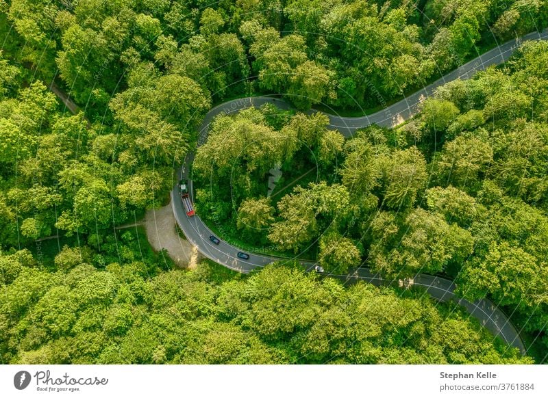 Aerial view of a green forest with a tractor on its leading through street slowing a row of cars behind it - traffic jam at a beautiful travel day tour series