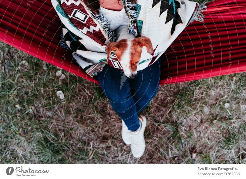 young woman relaxing with her dog in orange hammock. Covering with blanket. Camping outdoors. autumn season at sunset lying hammock jack russell pet nature park