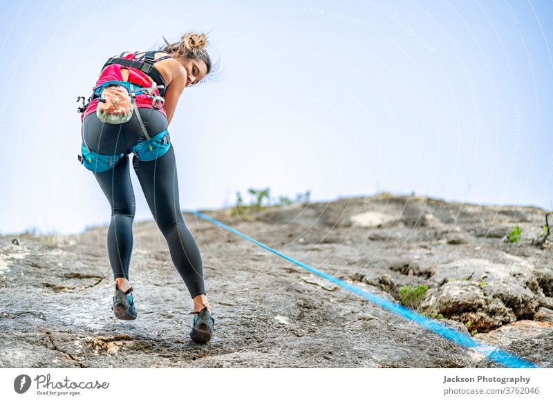 A woman climbing a steep rock in climbing harness climber down active activity adrenaline alcoholic algarve cliff exercise extreme focused height high holding