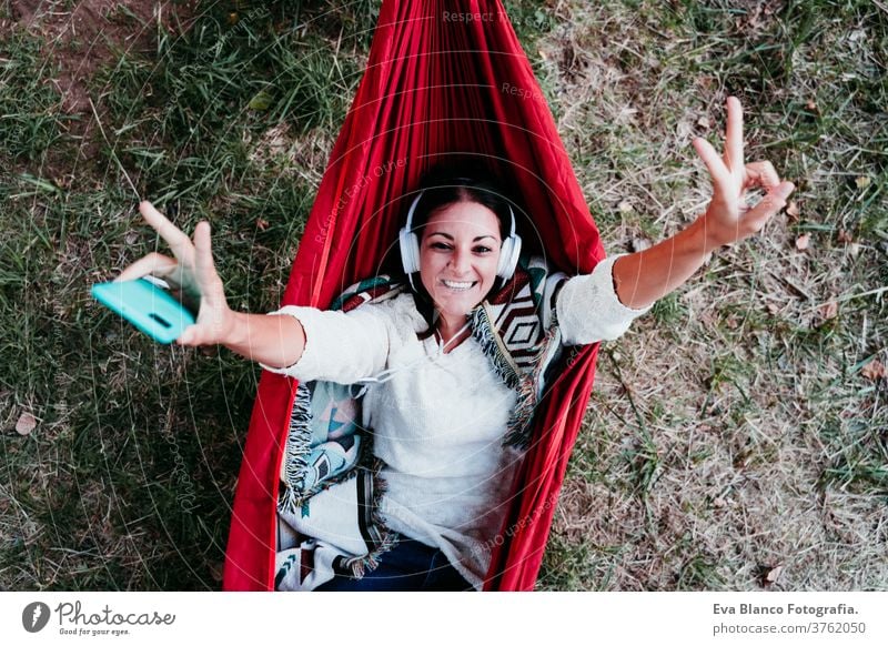 top view of happy woman relaxing in hammock and listening to music on mobile phone and headset. autumn season. camping concept earphones technology internet