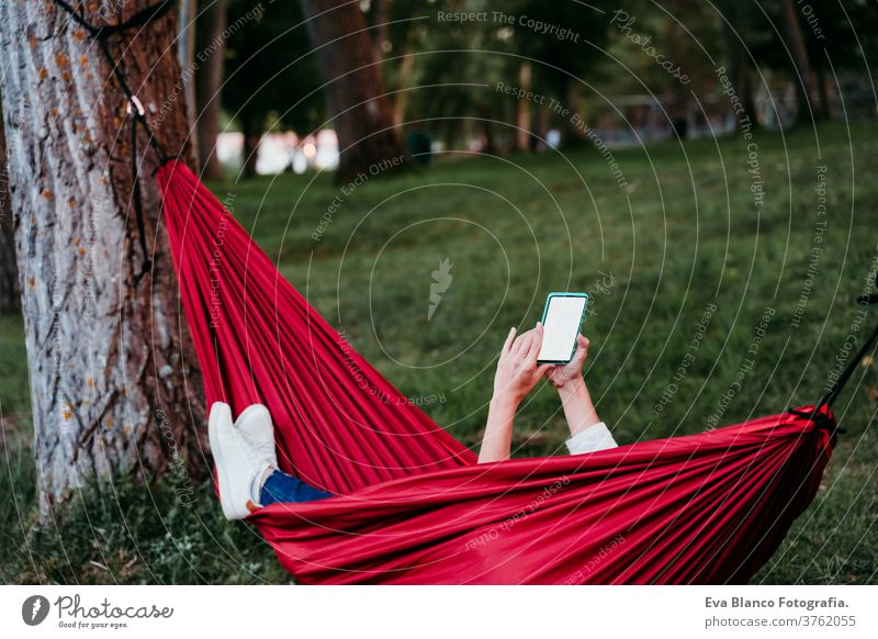 unrecognizable woman relaxing in orange hammock using mobile phone. Camping outdoors. autumn season at sunset headset earphones listening music technology