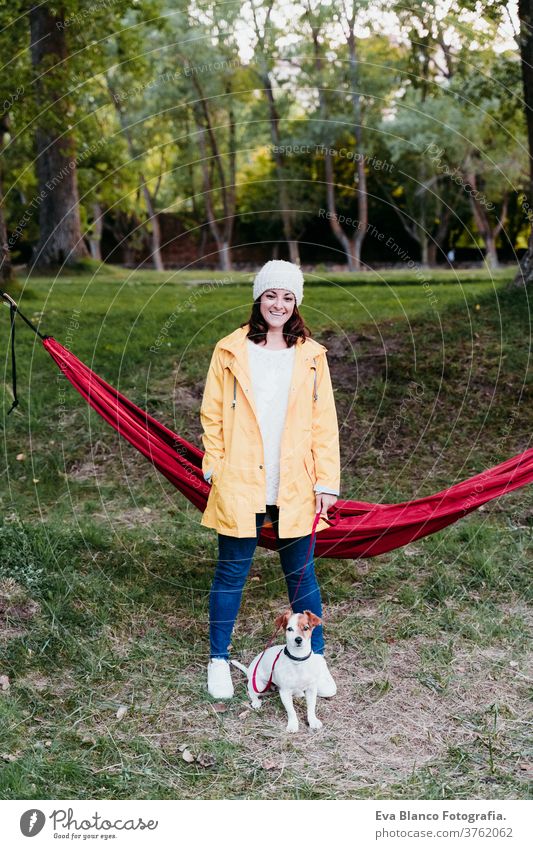 young woman wearing yellow raincoat standing next to hammock with her jack russell dog. autumn season. camping concept lying hammock pet outdoors nature sunset
