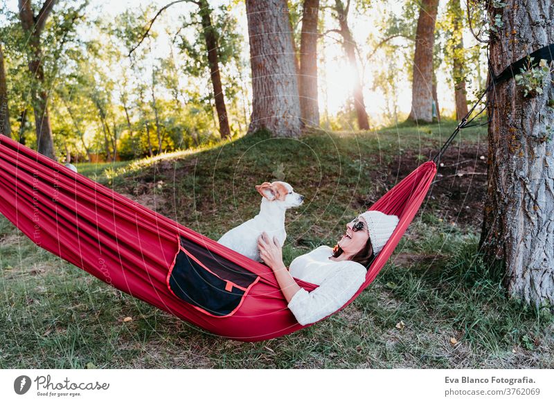 young woman relaxing with her dog in orange hammock. Camping outdoors. autumn season at sunset lying hammock jack russell pet nature park caucasian happy