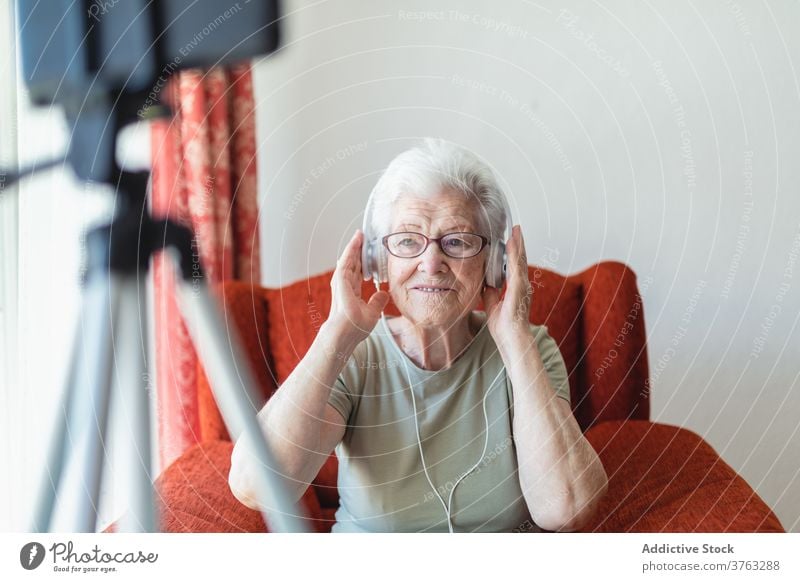Smiling elderly woman listening to music in headphones senior song enjoy relax home female delight armchair cozy sit cheerful happy comfort peaceful calm glad