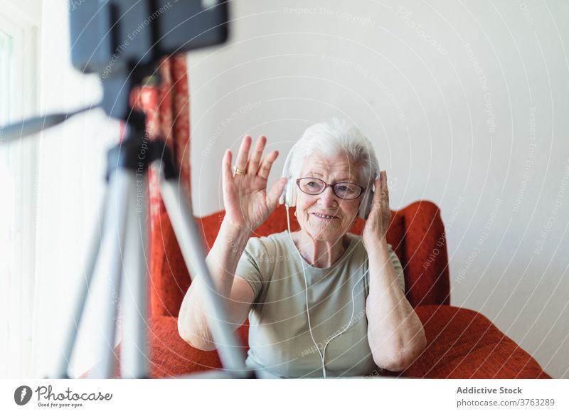 Elderly woman having video call with headphones senior listen music elderly song enjoy relax home delight armchair cozy sit comfort peaceful calm glad sound
