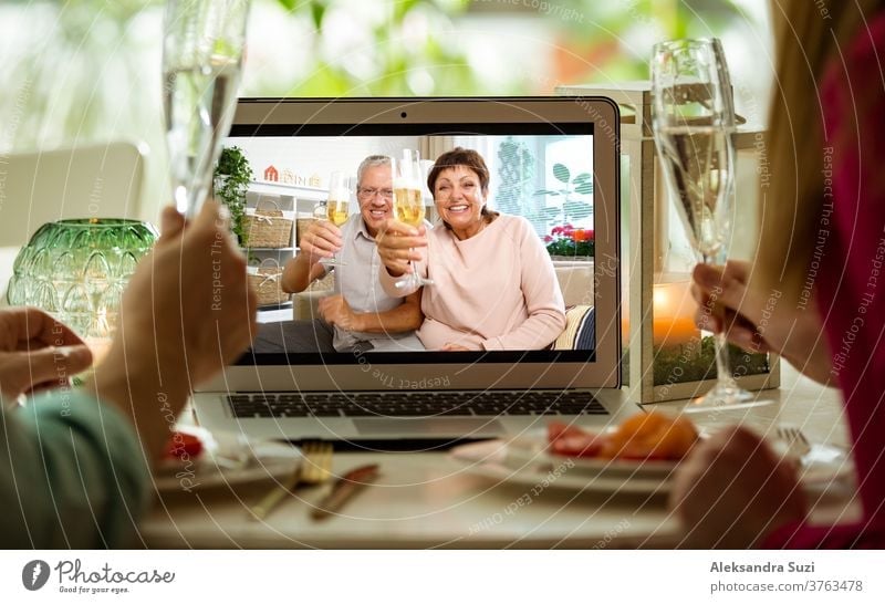 Man and woman sitting at the dining table, having dinner, drinking Champagne and having video call with senior parents on laptop. Staying home, quarantine and social distancing celebration of event.