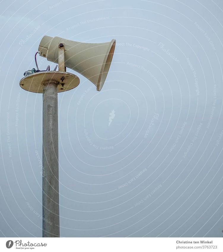Side view of an older loudspeaker in the shape of a megaphone in front of a bluish hazy sky Loudspeaker Megaphone Pole Sky announcement Communicate Information