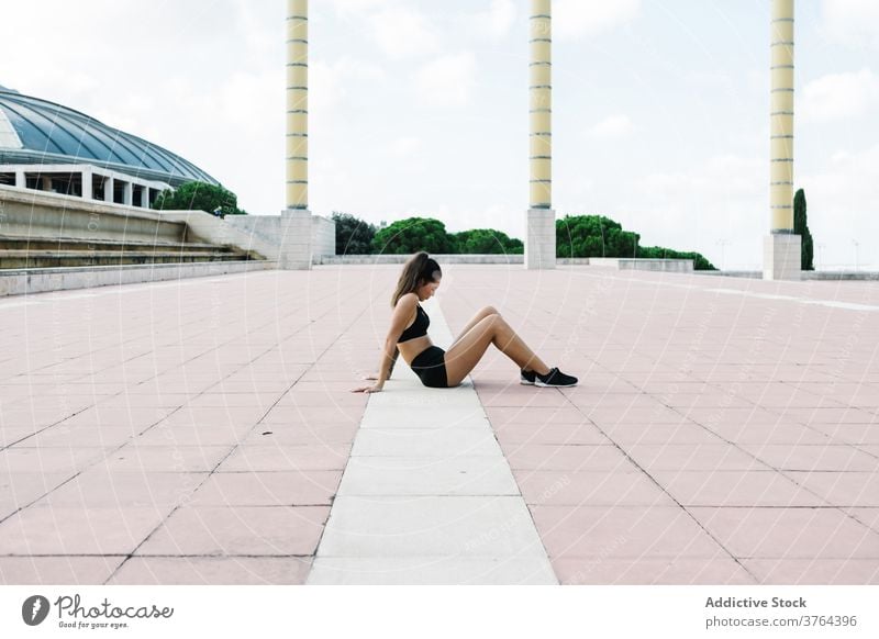 Fit woman in sportswear resting after training on city square fit relax street workout break fitness urban recreation tired exercise athlete sportswoman female