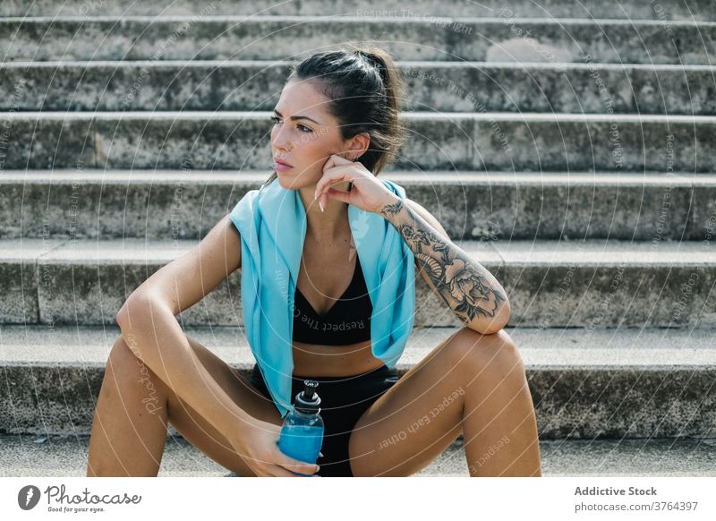 Tired sportswoman drinking water on stairs training rest refresh step workout tired exercise break hydrate refreshment beverage street athlete relax fit female