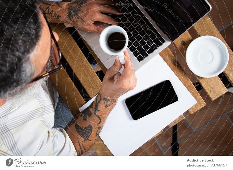 Busy man with cup of coffee working on laptop workplace busy using browsing drink gadget work from home casual male device freelance tattoo online internet