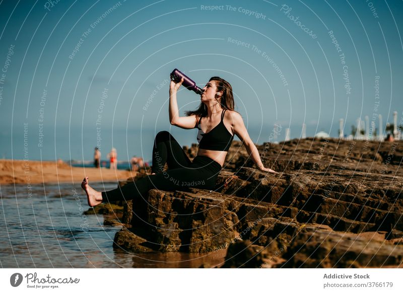 Tranquil woman sitting drinking water after yoga shore padmasana zen female stress relief stone sportswear wellness tranquil peaceful harmony practice relax