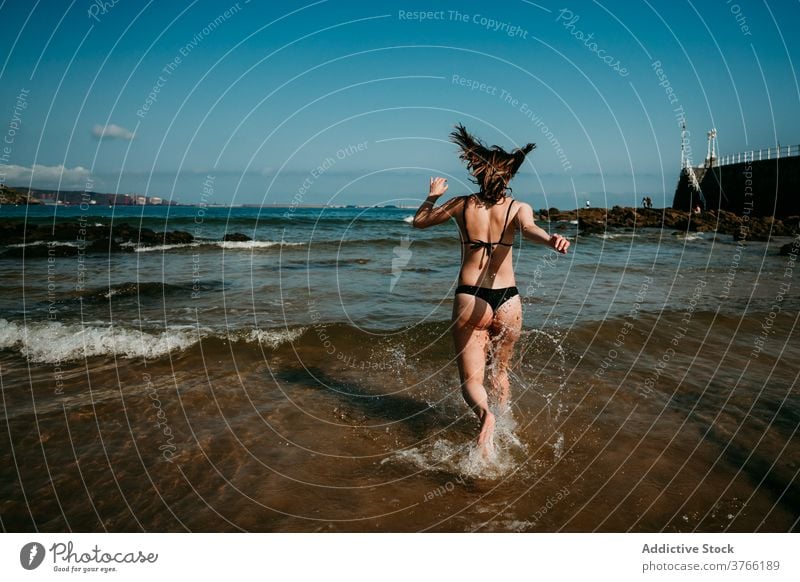 Anonymous carefree woman running in sea water having fun splash summer vacation holiday bikini female shallow resort relax happy nature rest young delight