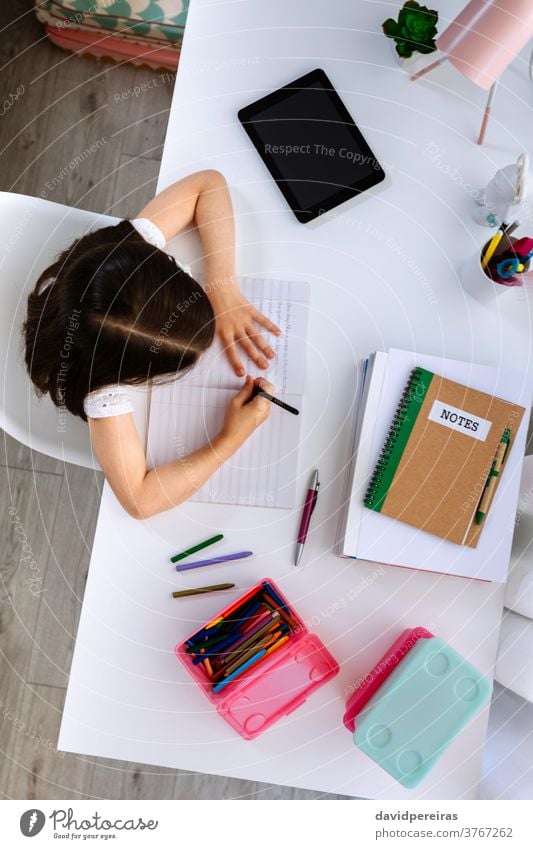 Girl doing homework sitting at a desk top view girl unrecognizable writing school education concentrated child overhead school at home book homeschooling room