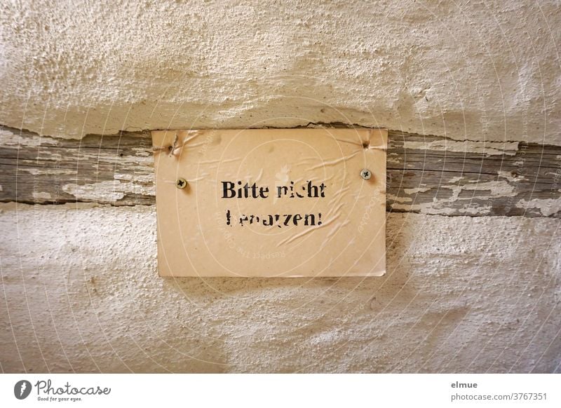 "Please do not use" is written illegibly in black print on a yellowed piece of paper attached to a wooden beam on an old wall. interdiction Piece of paper
