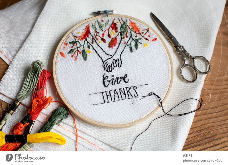 Handmade embroidery with Thanksgiving theme in a hoop thanksgiving illustration text give thanks holding hands leaves tree concept idea embroidery hoop gift DIY