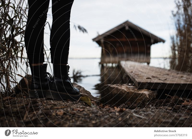 Anonymous traveler standing near pier at lakeside in autumn day woman shed gloomy lonely leg shore nature calm tranquil female tourism germany austria boot