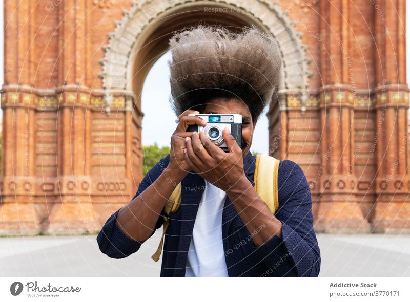 Black man taking a picture while facing the camera with a camera journalist lens stock fashionable trendy hobby photography stylish creativity men shot eye