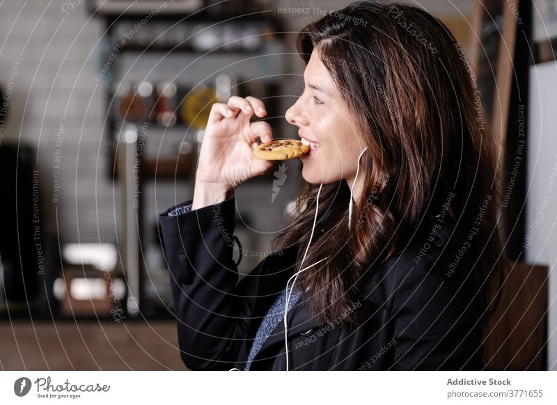 Delighted woman listening to music in cafe carefree enjoy eat cookie smartphone earphones female delicious food weekend gadget happy pleasure dessert sit yummy