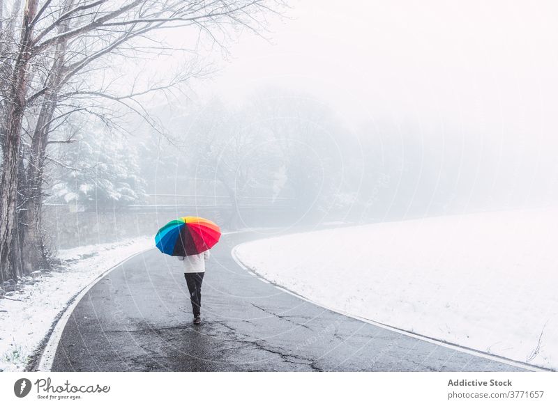 Unrecognizable person walking along road in winter park colorful umbrella snow snowfall cold season pyrenees catalonia spain weather frost holiday vacation